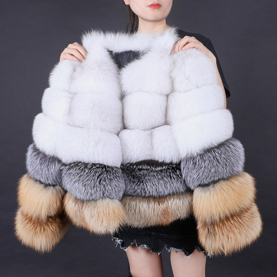 Multicolored fur vest with white, gray, and brown accents held by a person against a dark background.
