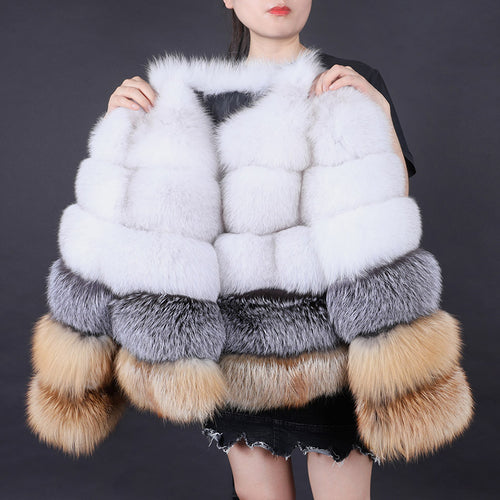 Multicolored fur vest with white, gray, and brown accents held by a person against a dark background.