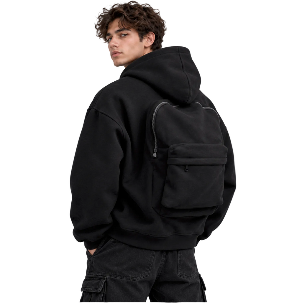 A man wearing a black hoodie and black cargo pants, shown from the back while wearing a black backpack with multiple front pockets, against a solid gray studio background.