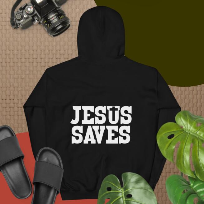 Black hoodie with 'JESUS SAVES' text on a textured surface with camera, sandals, and plant.