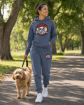 Woman wearing a shale blue BE UP FOR LIFE French terry jogger set while walking a small dog in a park.
