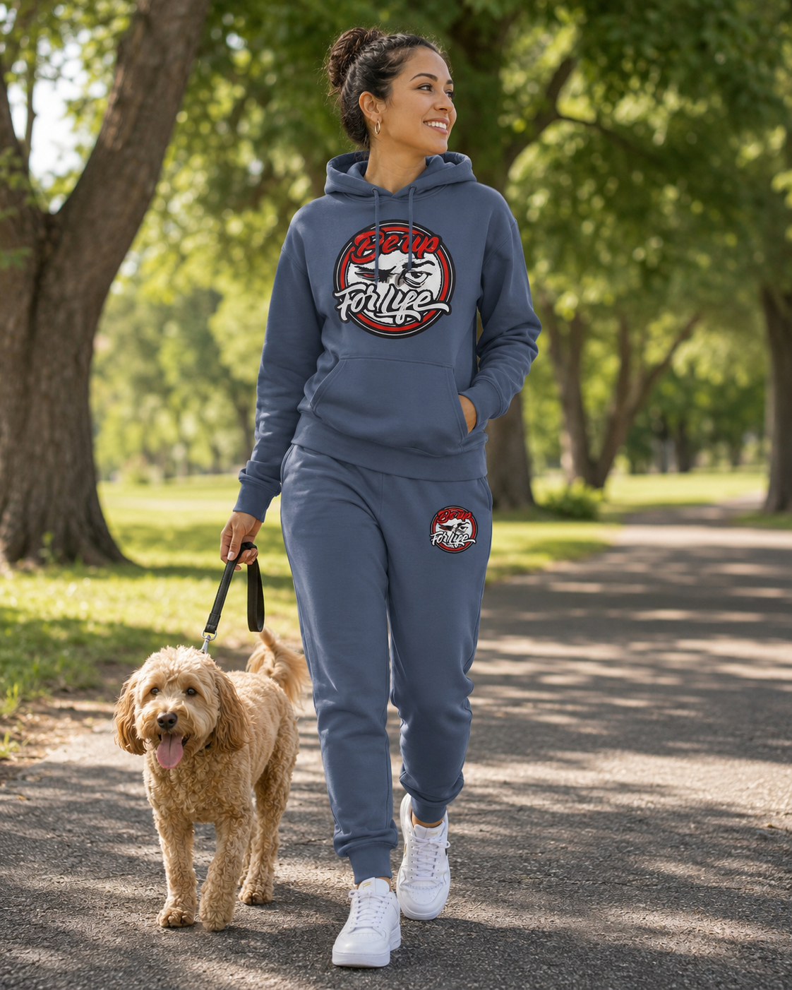 Woman wearing a shale blue BE UP FOR LIFE French terry jogger set while walking a small dog in a park.
