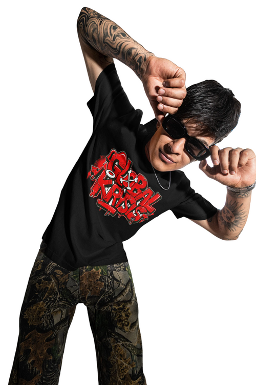 Person wearing a black t-shirt with Global Krysis red graphics and camouflage pants, standing in a room with large windows overlooking a cityscape.