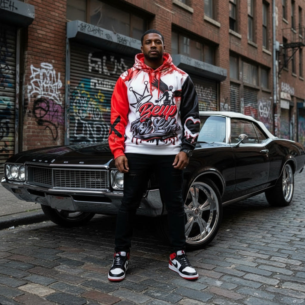 Man in a hoodie standing next to a classic car on a street with graffiti.