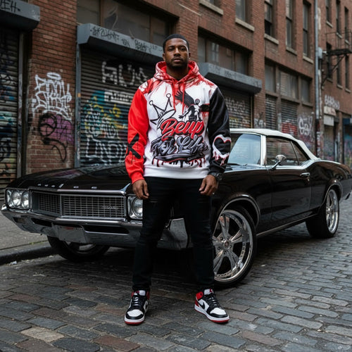 Man in a hoodie standing next to a classic car on a street with graffiti.